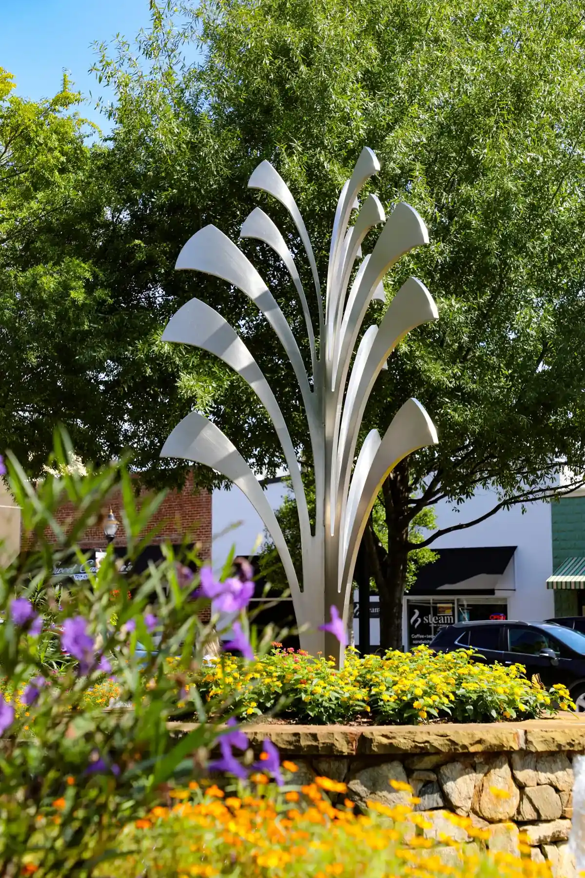 Downtown Fountain Inn public art framed by flowers, green trees, and Main Street storefronts