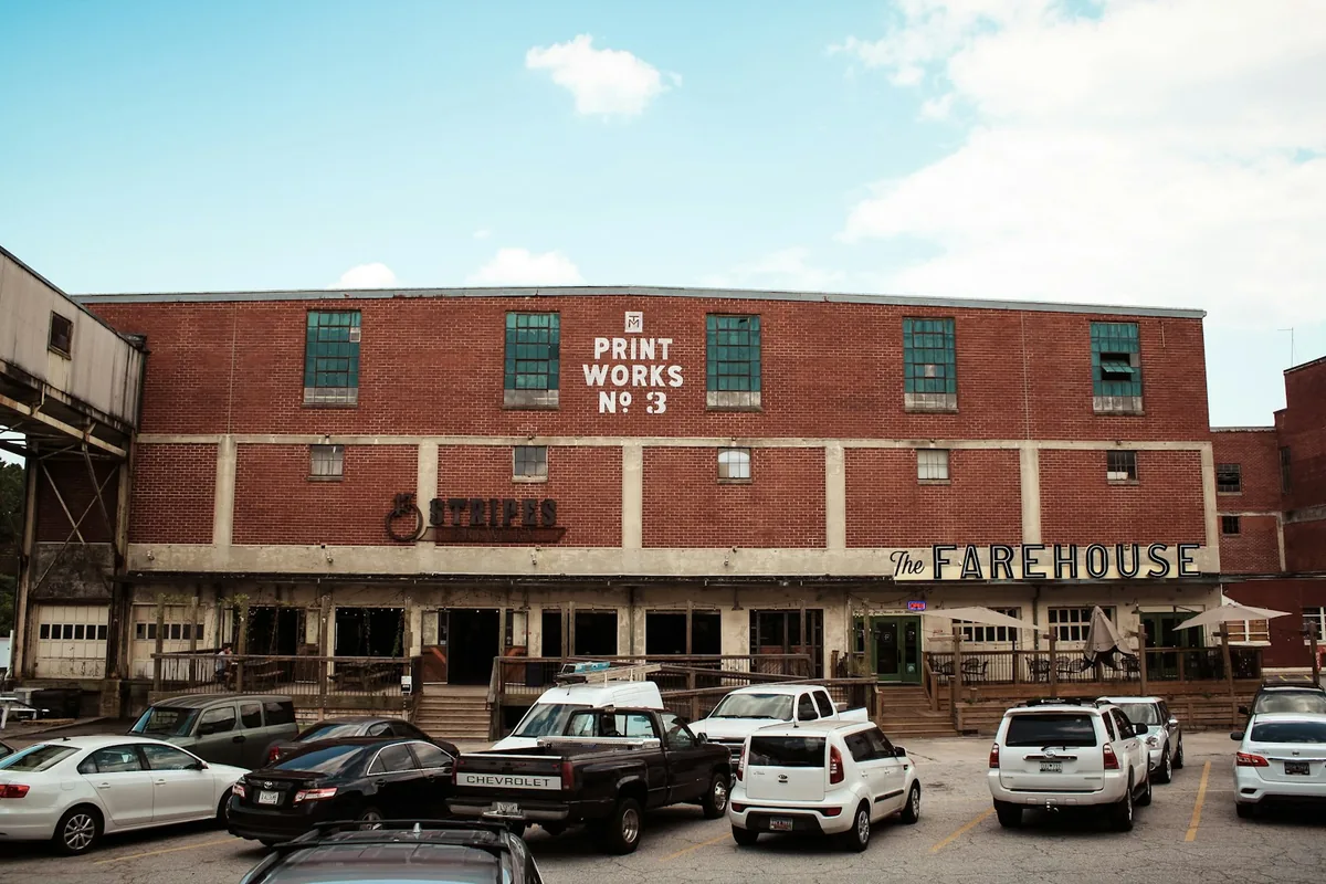 Red brick Print Works No. 3 building at Taylors Mill, with restaurants, tall windows, and a blue sky
